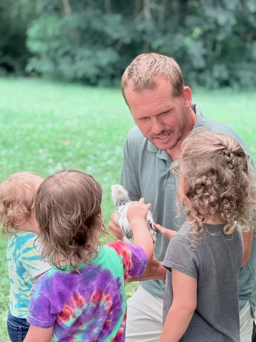 Ben helping children meet a chicken outdoors